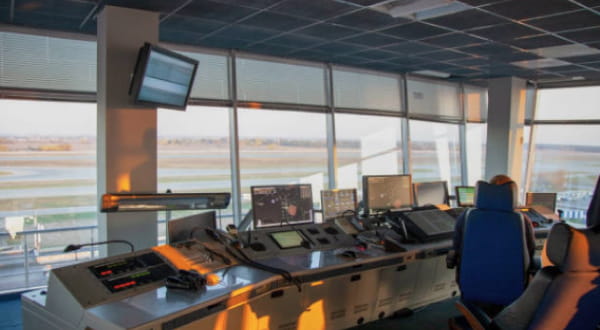 Interior view of an air traffic control tower with various control panels and screens, overlooking a runway